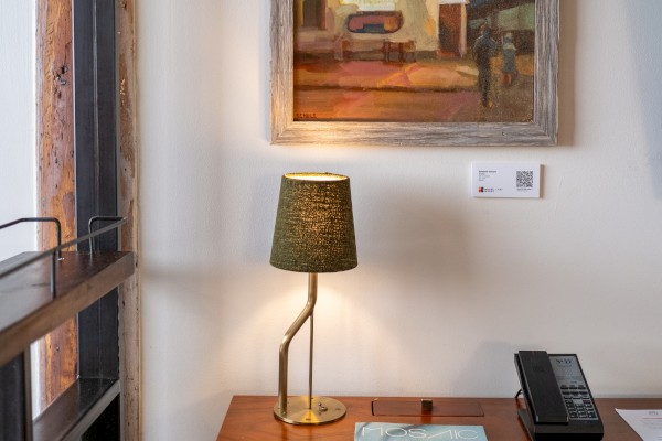 A cozy desk area with a lamp, framed artwork, chair, and a rotary phone on a wooden desk.