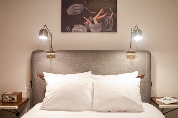 A neatly made bed with white pillows and a grey headboard is flanked by two bedside tables, each under a wall-mounted lamp.