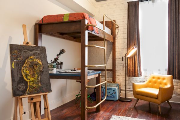 The image shows a cozy room with a loft bed, an art station with a painting on an easel, a yellow chair, and a suitcase near the window.