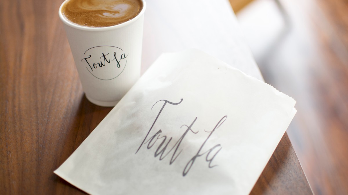 A latte in a cup and a paper bag with the same cursive text 