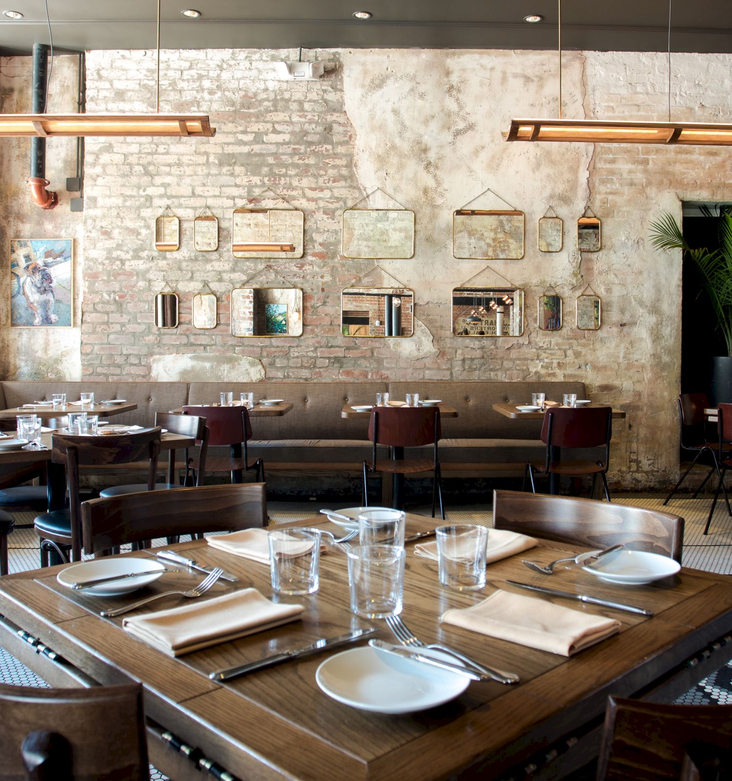 This image shows a stylish restaurant interior with neatly set tables, vintage decor on the exposed brick wall, and a cozy, inviting atmosphere.