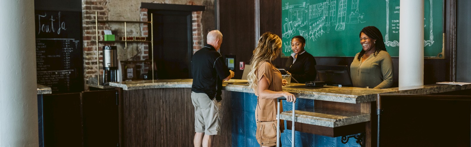 This image shows two hotel guests checking in at the front desk while two receptionists assist them.