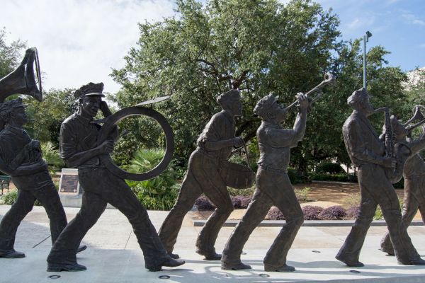 Bronze statues of a marching band with various instruments are displayed outdoors with trees and a clear sky in the background.
