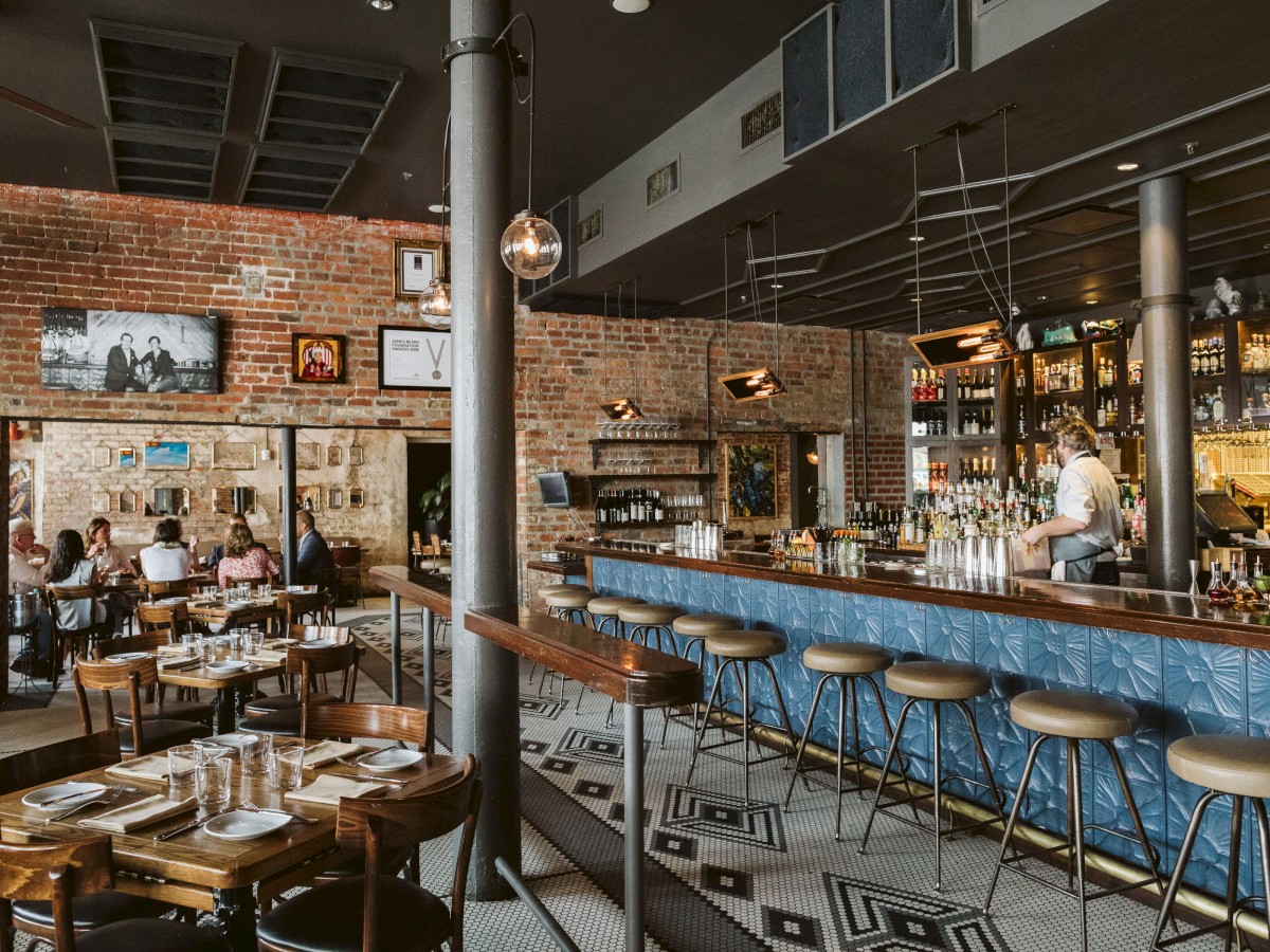 The image shows a cozy restaurant with a bar, stools, tables, and people dining, creating a warm and inviting atmosphere.