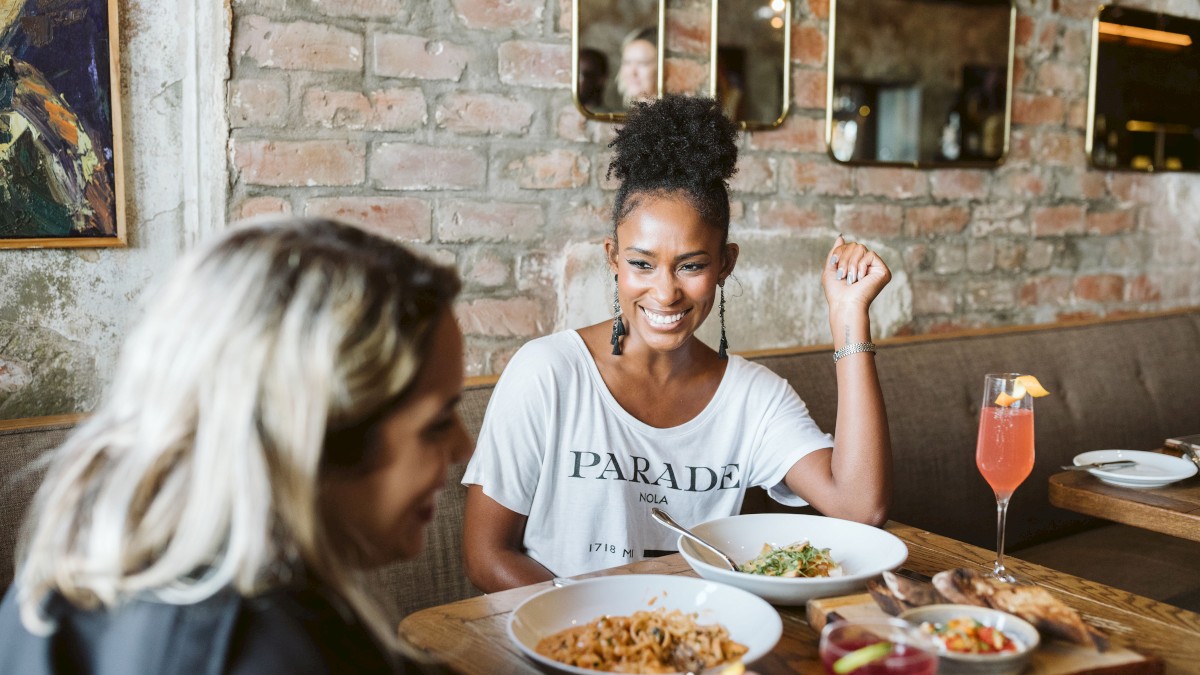 Two people are dining at a restaurant, enjoying meals and drinks in a cozy setting with brick walls and stylish decor.