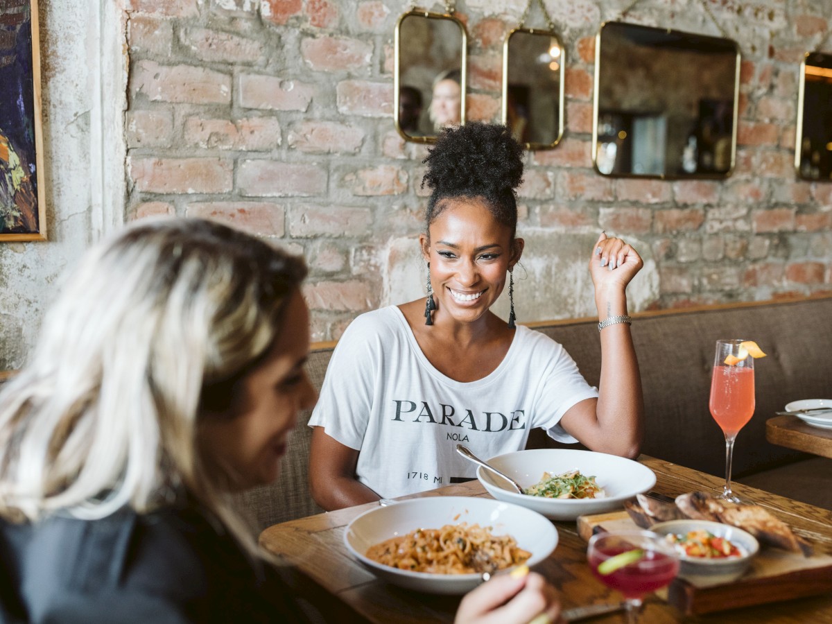 Two people are dining at a restaurant, enjoying meals and drinks in a cozy setting with brick walls and stylish decor.