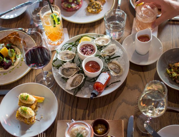A table set with various dishes including oysters, drinks, and appetizers. The table is wooden, adding a rustic touch to the dining experience.