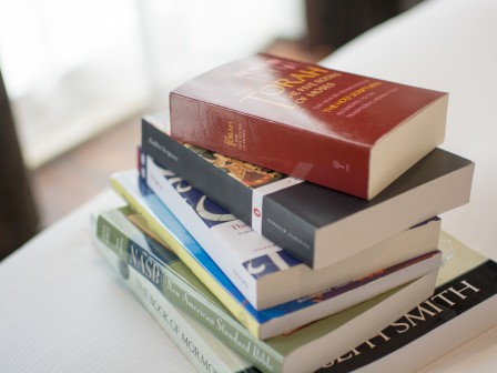 A stack of seven books is placed on a white surface, including a red-covered book titled 