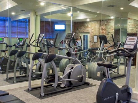 A modern gym with exercise equipment including ellipticals, stationary bikes, and benches, surrounded by mirrors on the walls.