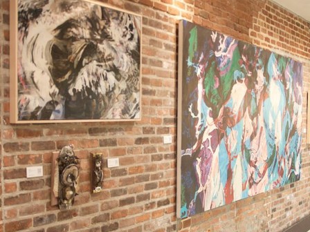 The image shows a brick wall displaying two abstract paintings and two antique-looking pieces hanging between them.