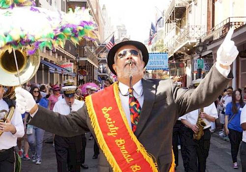 A man leads a brass band parade through a lively street crowd.