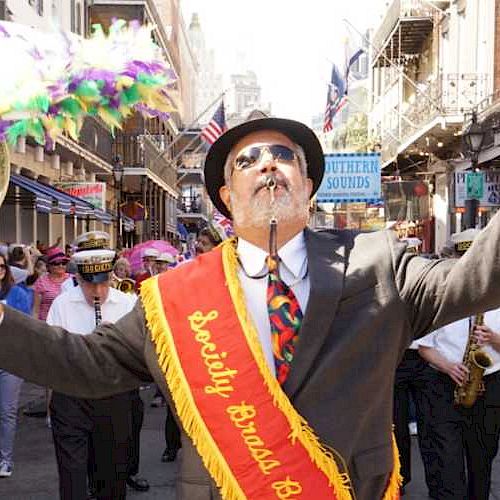 A man leads a brass band parade through a lively street crowd.