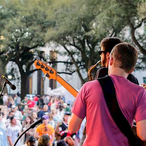 Band performing live on stage viewed from behind, facing an audience outdoors.