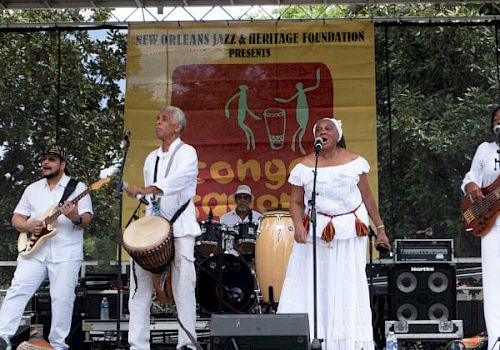 A band performs on stage at a music event, with instruments and speakers visible.