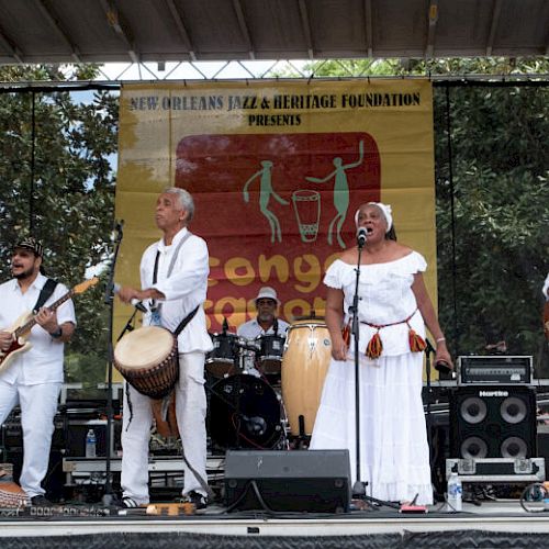 A band performs on stage at a music event, with instruments and speakers visible.