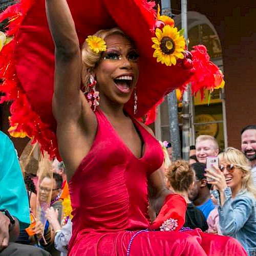 Three people in festive attire are on a gay LBGTI parade float, cheering with a crowd around