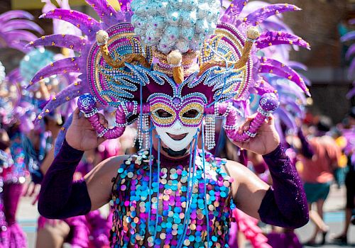 A person in a vibrant carnival costume with a mask and feathers.