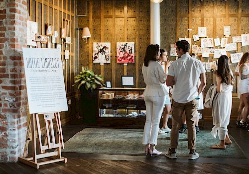 People at an event with artwork displayed on walls and easel signage.