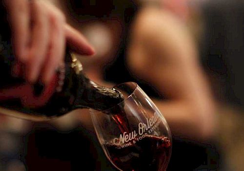 A person's hand is pouring red wine into a glass with a logo.