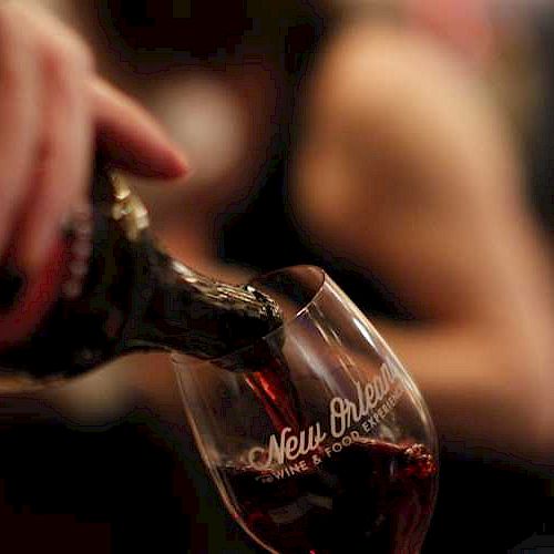 A person's hand is pouring red wine into a glass with a logo.