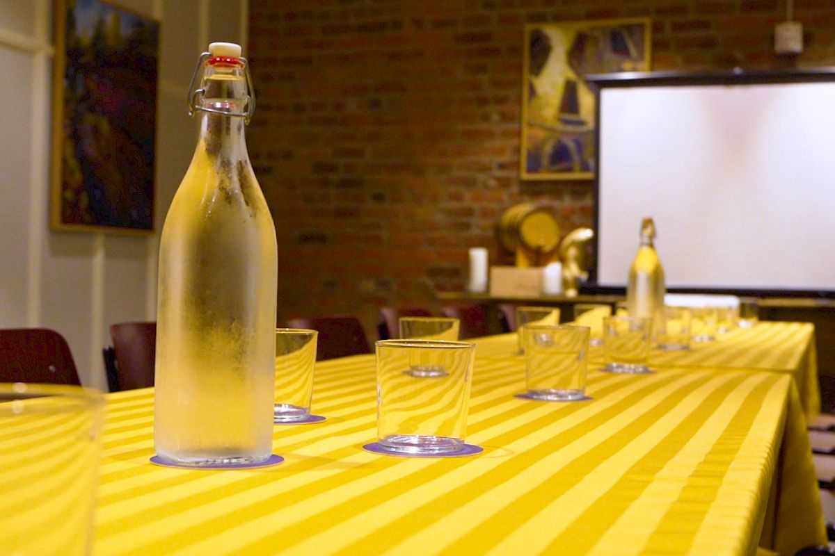 A long table with a yellow striped tablecloth, glasses, and water bottles is set up in a room with a projector and paintings on the walls.