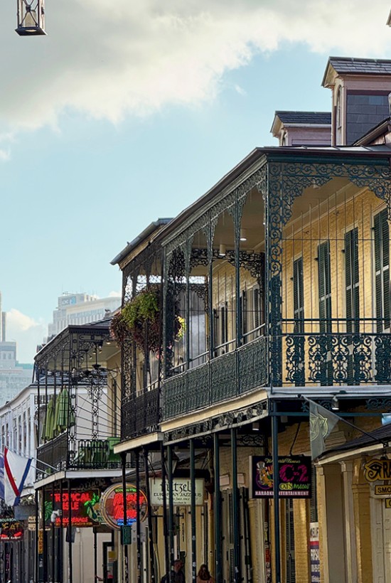 A street in New Orleans featuring historic buildings with ornate iron balconies under a cloudy sky.