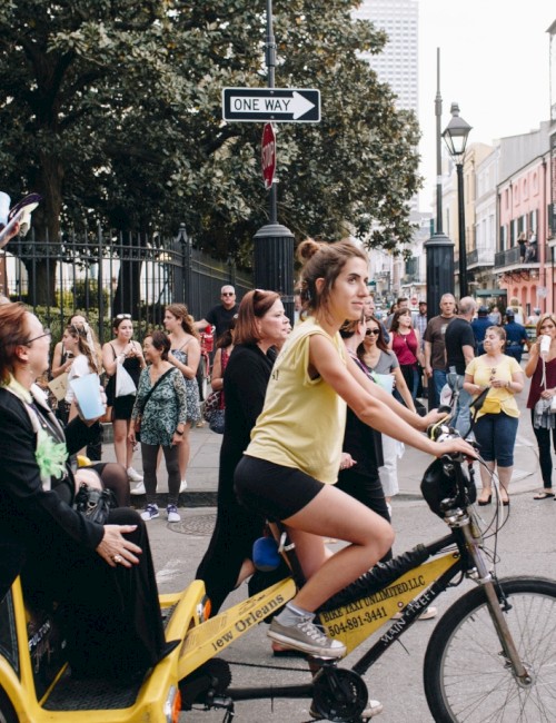 A woman pedals a bike taxi carrying passengers through a street bustling with pedestrians.