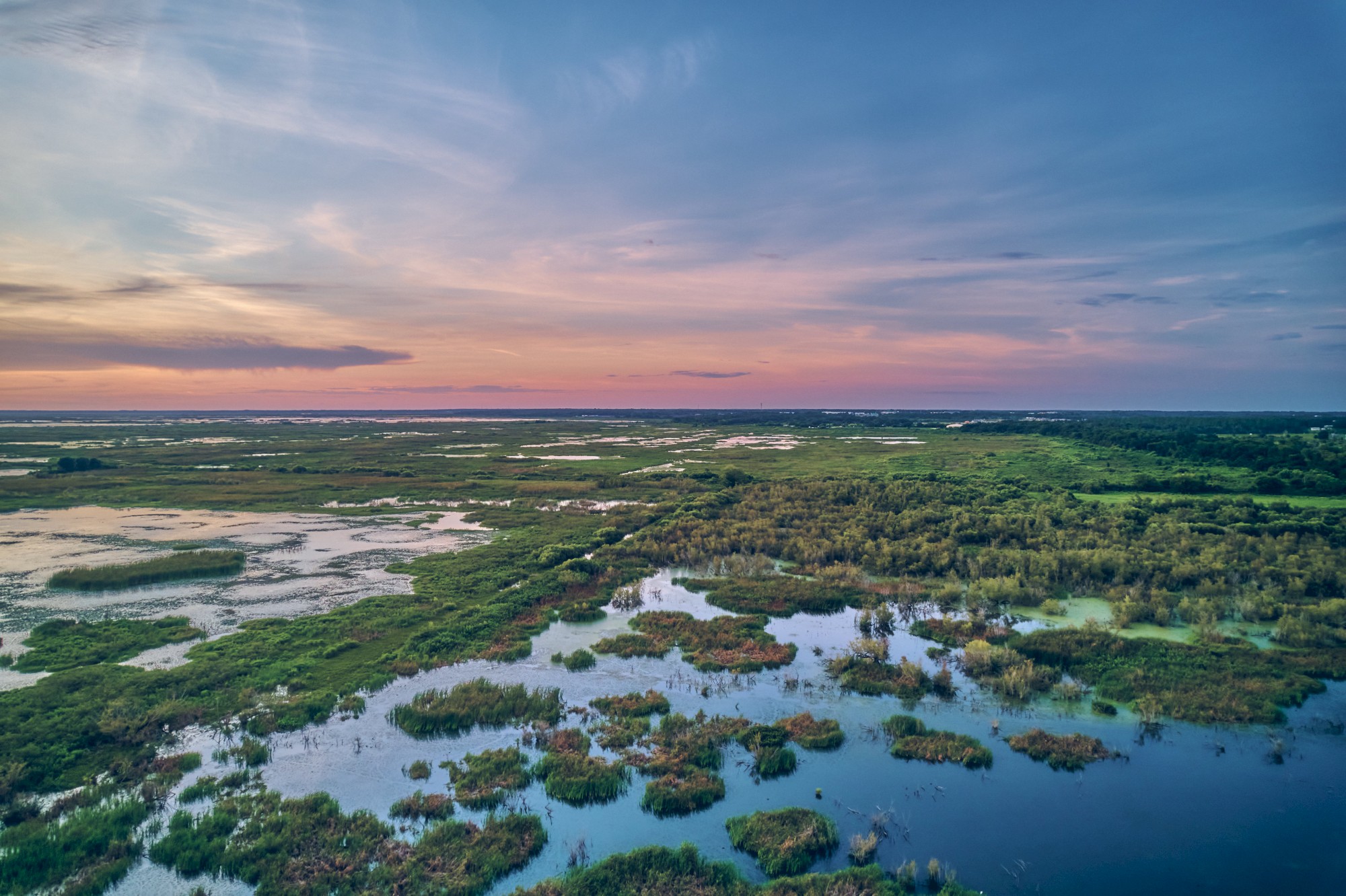 The image depicts a scenic landscape of wetlands with water, vegetation, and a colorful sky at sunset.