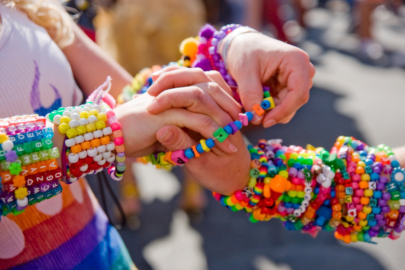 The image shows two people exchanging colorful beaded bracelets outdoors, with both wearing several bracelets on their arms.