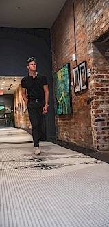 A person walks down a corridor with brick walls, featuring framed artwork on display.