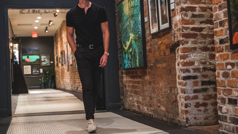 A person is walking down a hallway with brick walls, featuring art pieces displayed on each side.