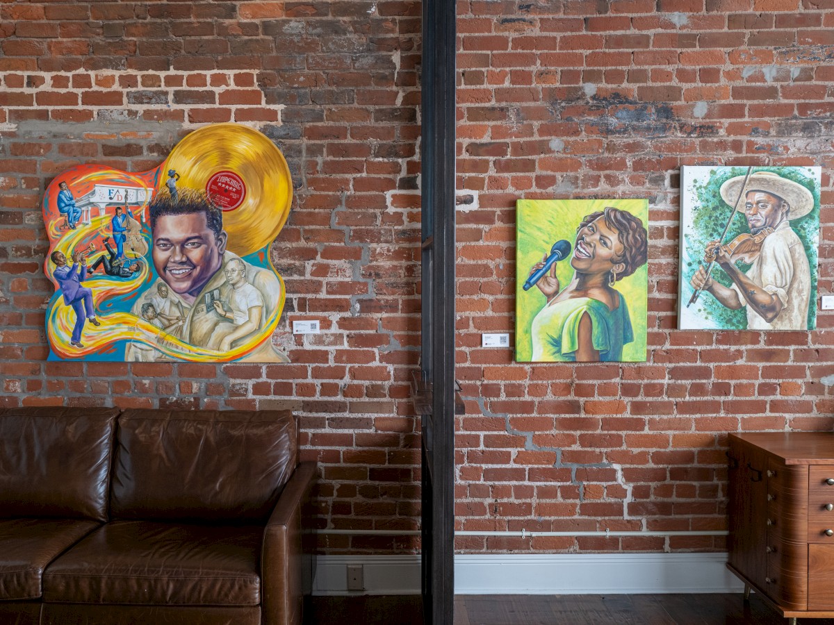 The image shows a brick wall with colorful paintings, a brown leather couch, and a wooden cabinet.