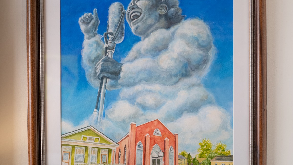 A framed painting of a cloud shaped like a person singing into a microphone above a landscape with colorful buildings and small figures.