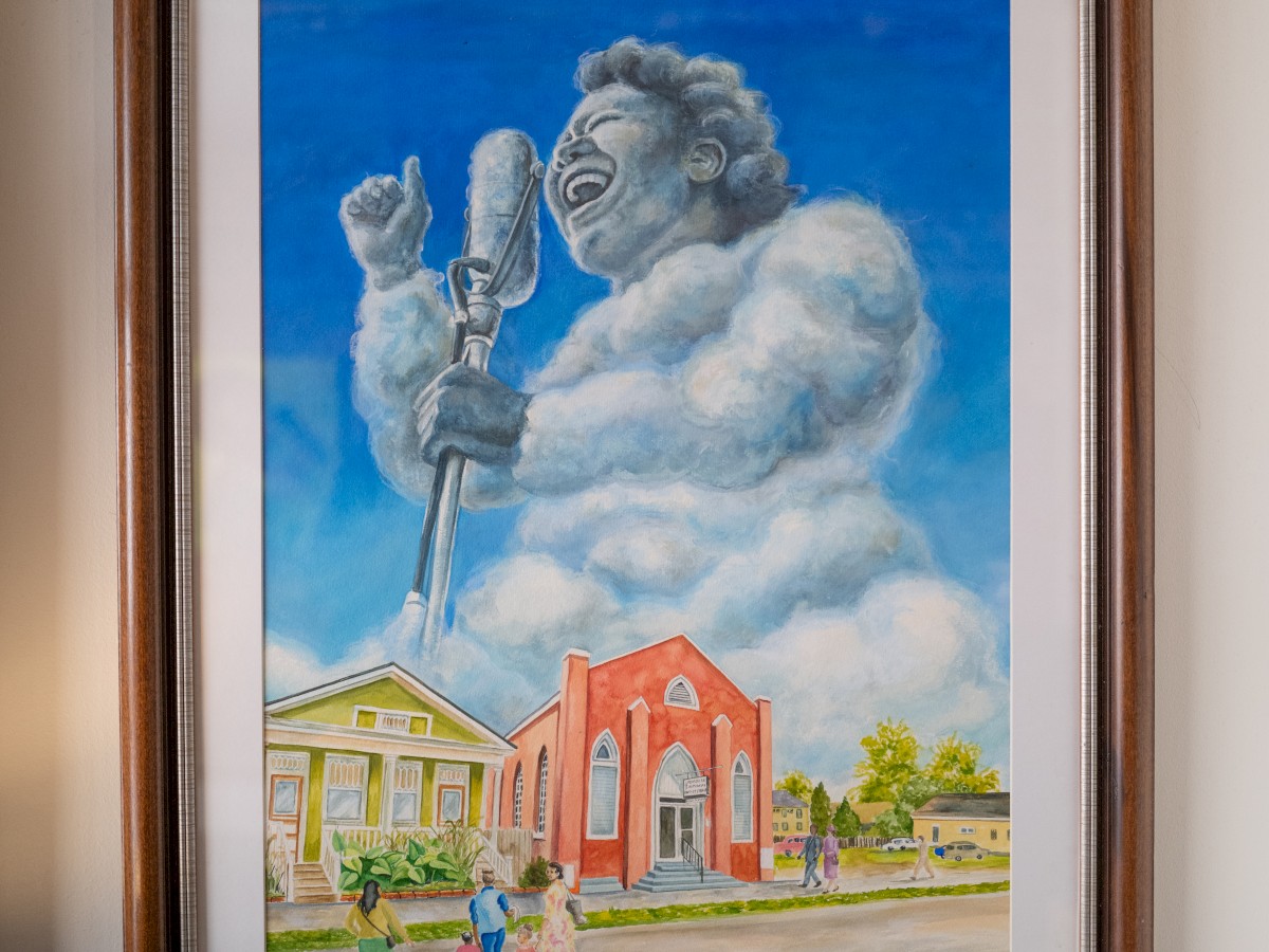 A framed painting of a cloud shaped like a person singing into a microphone above a landscape with colorful buildings and small figures.