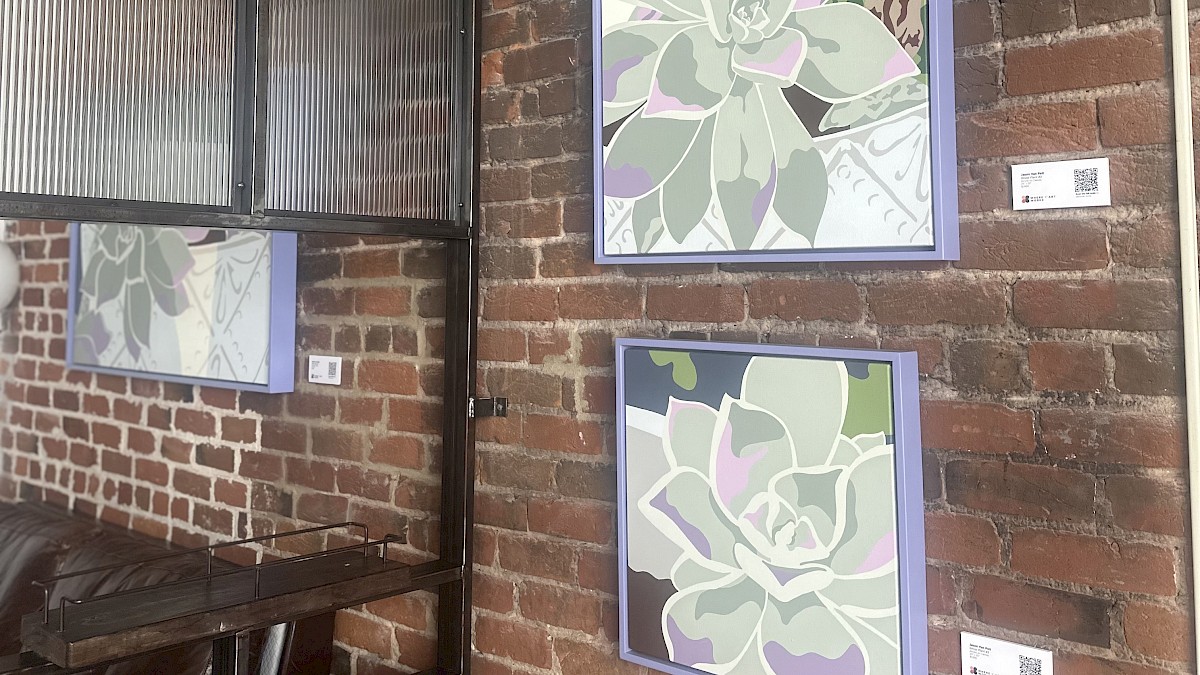 Two framed abstract succulent plant artworks are hung on a brick wall in an indoor space.
