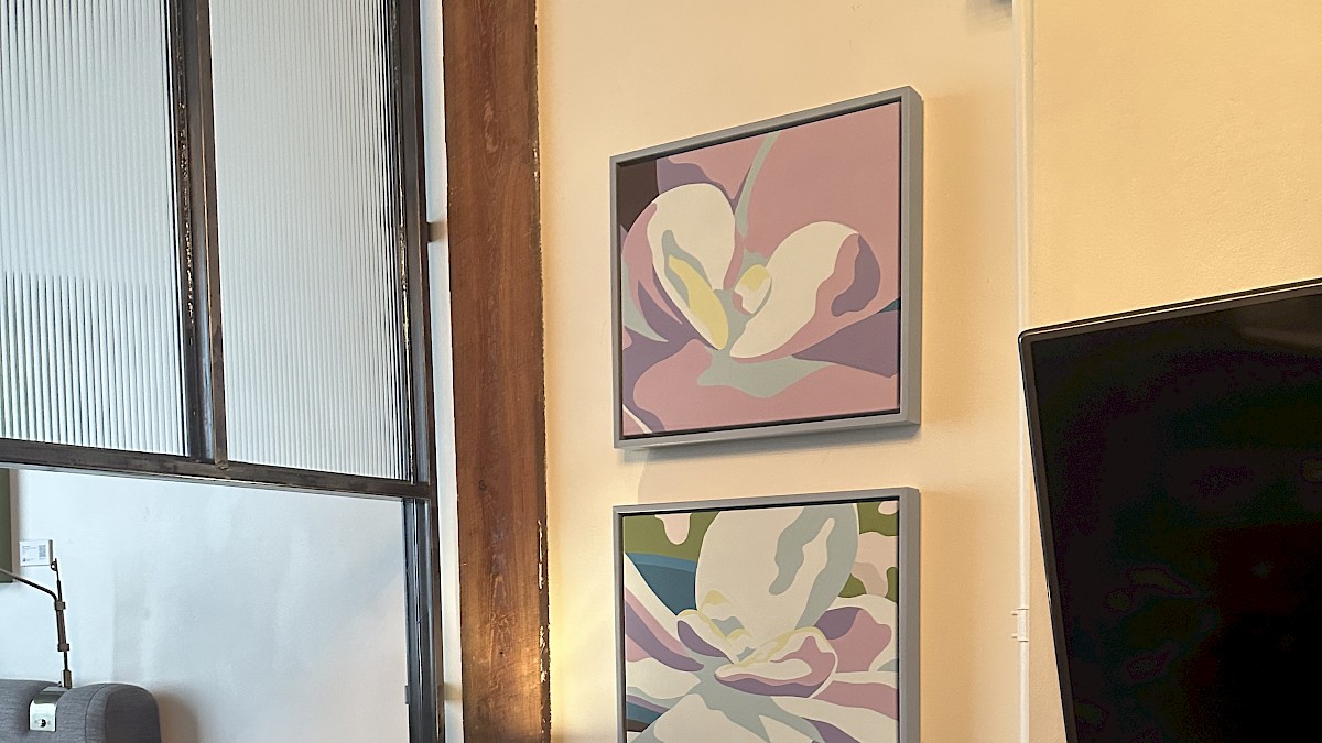 A cozy desk setup in a room with two colorful flower paintings, a black telephone, and a small lamp on a wooden table.