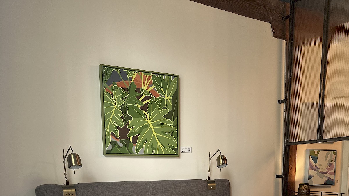 A neatly made bed with white sheets and pillows, above which hangs a green leafy artwork in a cozy, modern hotel room.