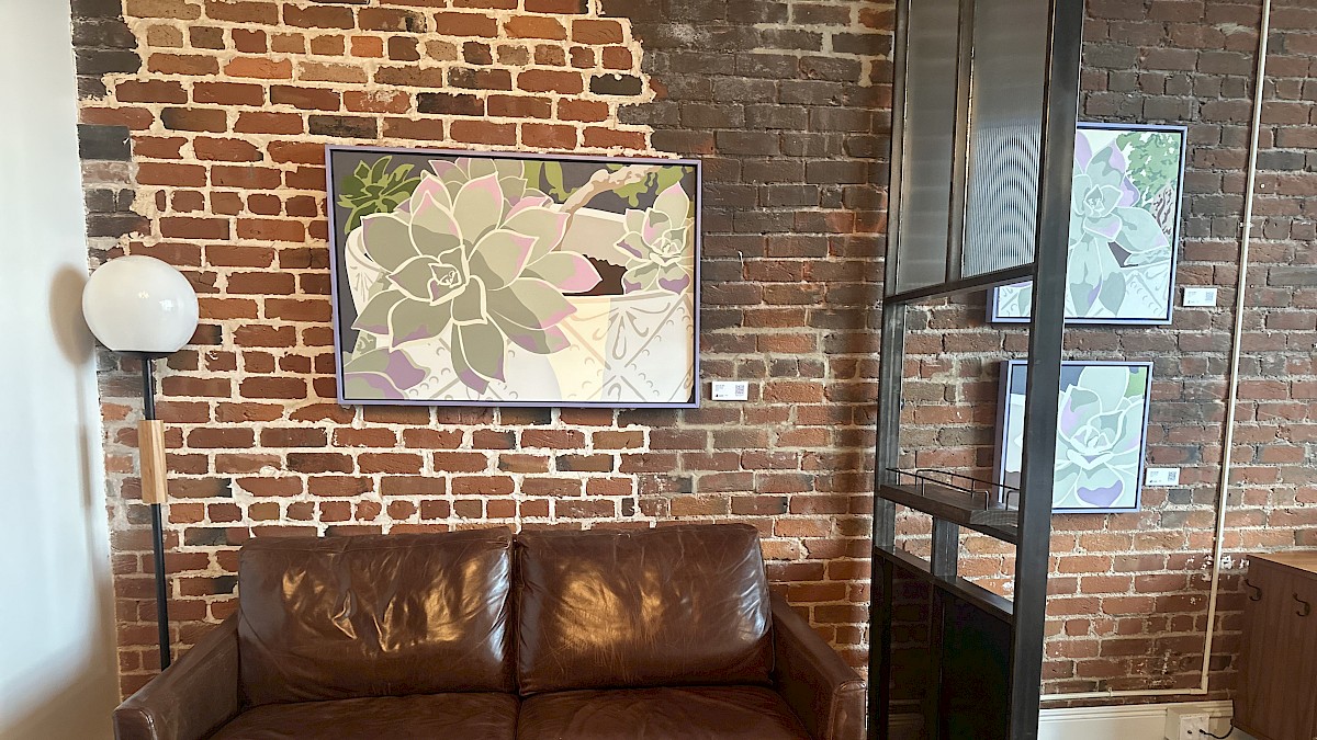 The image shows a cozy corner with a brown leather couch, galaxy-style artwork on a brick wall, a white globe lamp, and a black metal shelf.