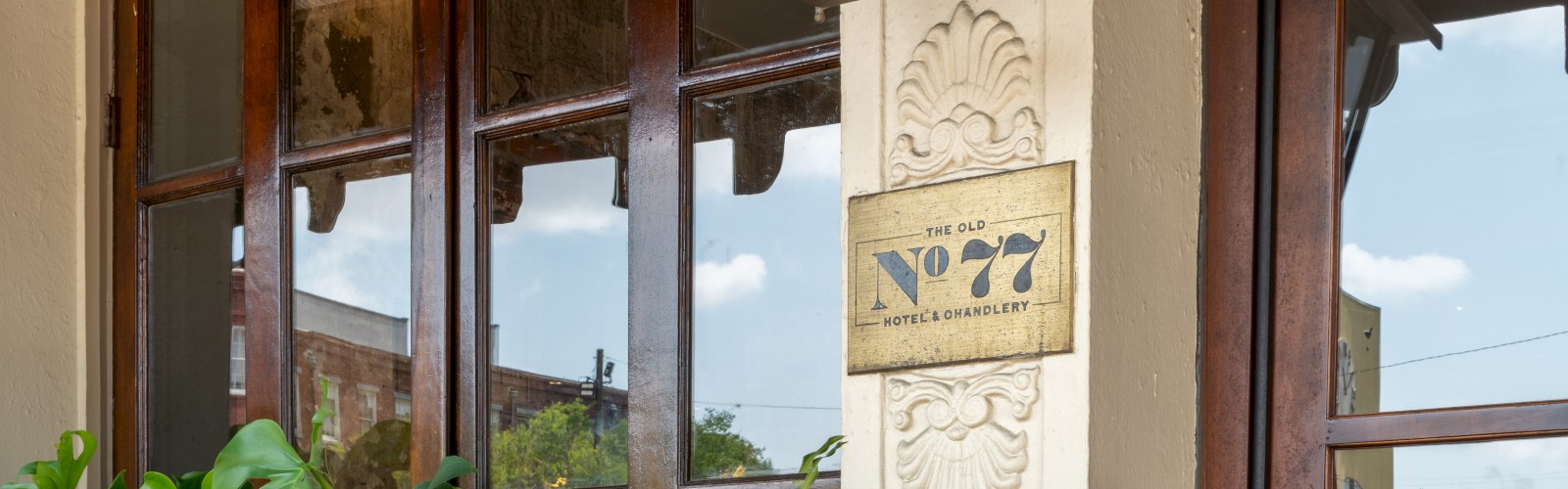 The image shows a building entrance with a vintage lamp, plants in pots, and a number plate reading 