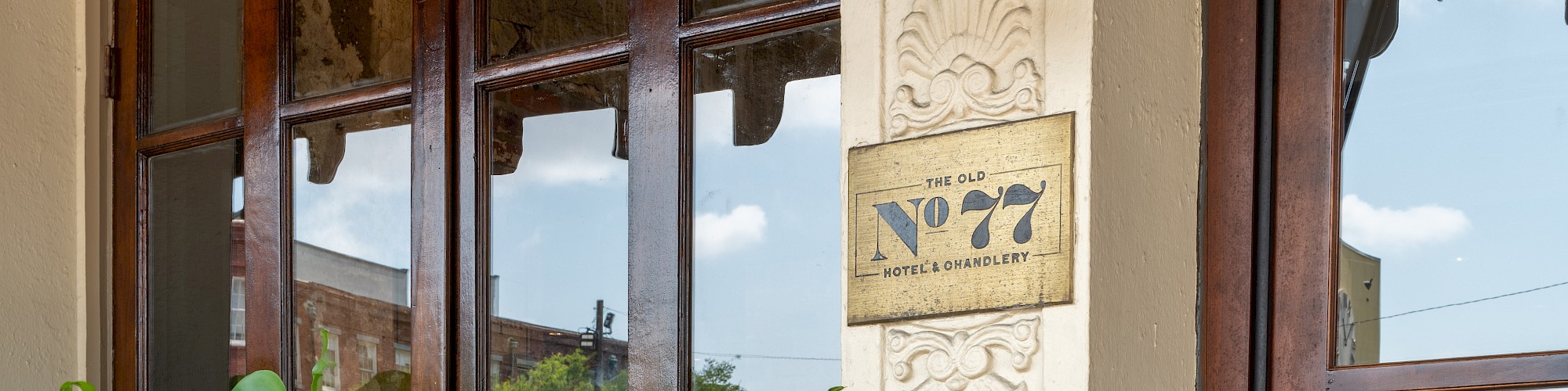 The image shows a building entrance with a vintage lamp, plants in pots, and a number plate reading 