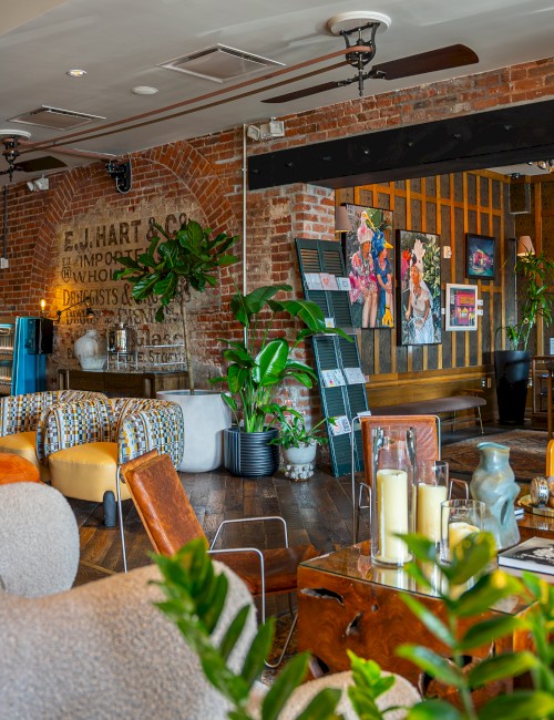 A cozy, stylish café with brick walls, comfy seating, and plants, featuring eclectic decor and warm lighting.
