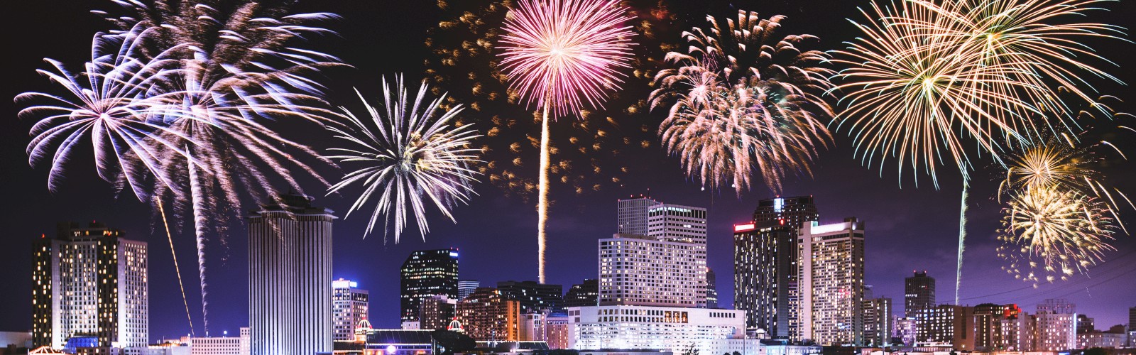 A city skyline at night with bright, colorful fireworks lighting up the sky, reflecting beautifully on a body of water.