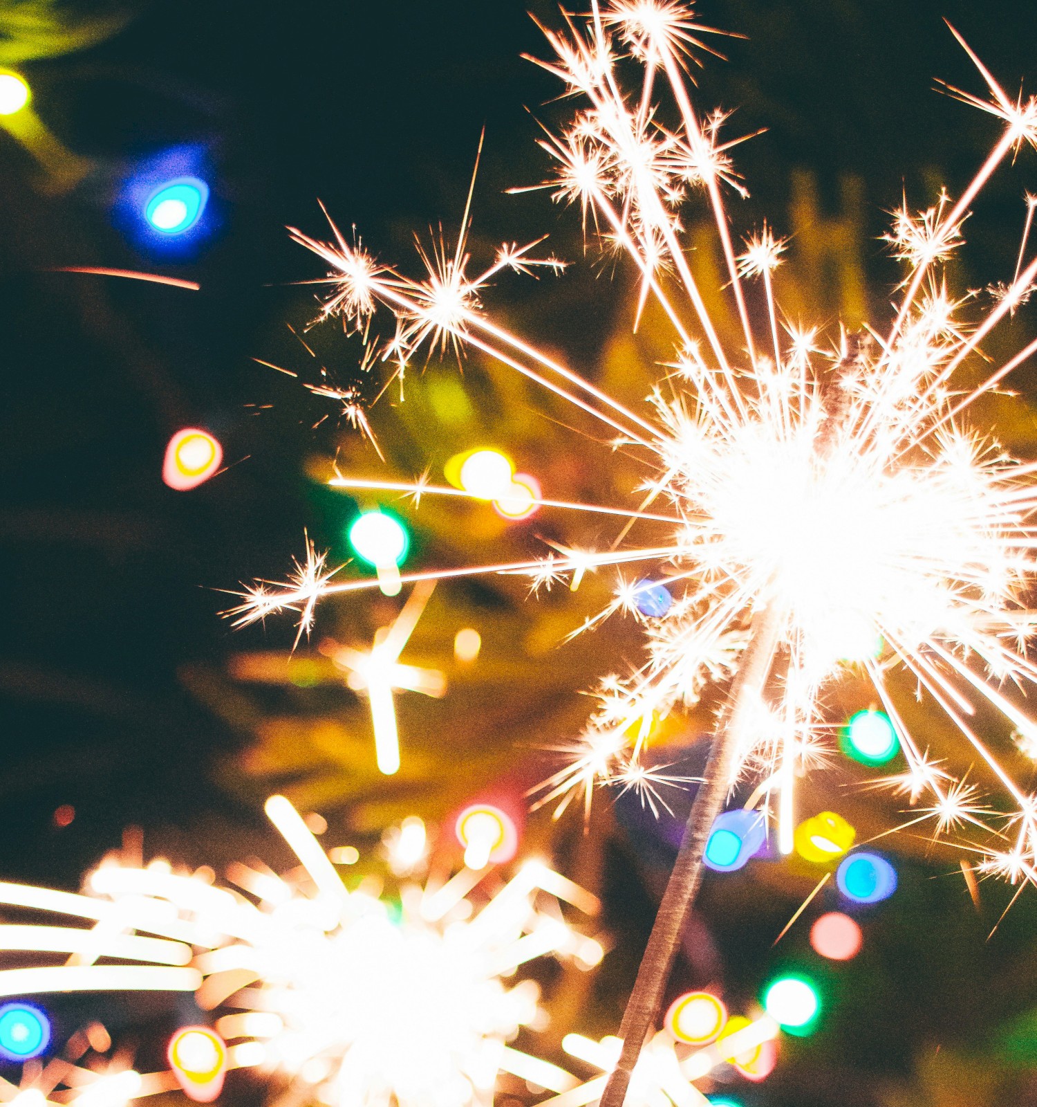 A sparkling firework sparkler with colorful lights blurred in the background creates a festive and vibrant scene.