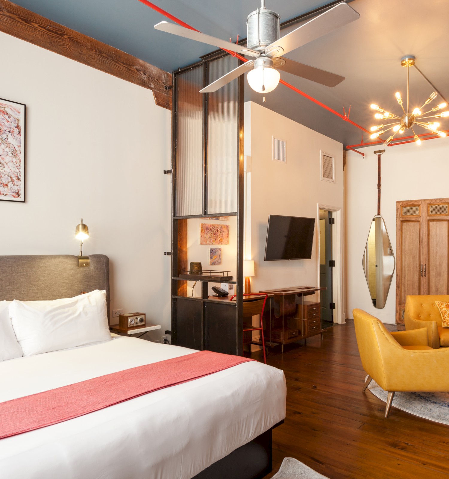 A stylish hotel room with a bed, two yellow chairs, a TV, and unique lighting, all set in a cozy modern decor.
