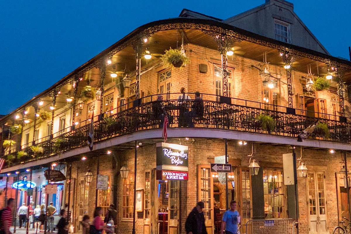 A lively street scene with a historic, lit-up building featuring a wraparound balcony at dusk.