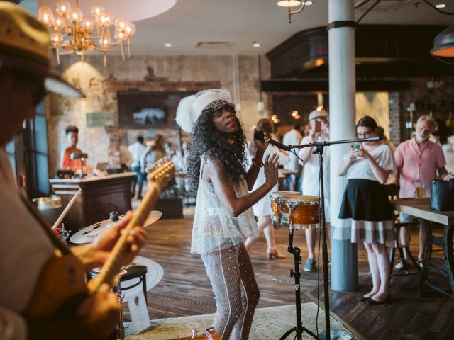 A lively indoor scene with a musician singing, a guitarist, and an audience enjoying the performance in a cozy setting.