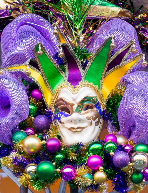 A festive Mardi Gras mask with purple, green, and gold feathers and beads, bright and celebratory.