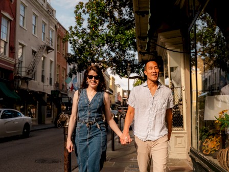 A couple walks hand in hand down a charming city sidewalk on a sunny day, enjoying each other's company.
