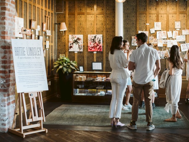 People viewing and discussing artwork at an art exhibition inside a gallery space.